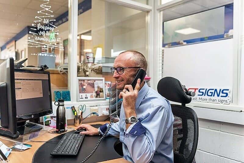 An image of a FASTSIGNS employee on the phone at a desk.